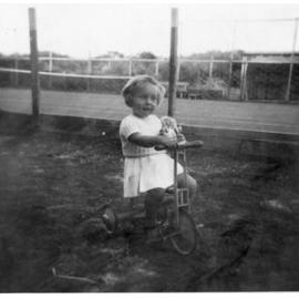 Christine Renston riding a bike with her doll outside Paringa Flats in Scarborough