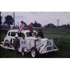 Children on on racing car with Gwelup School in background 
